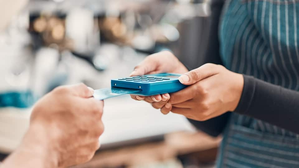 Closeup of credit card machine held by cashier and hand of customer paying for shopping using contactless card at checkout
